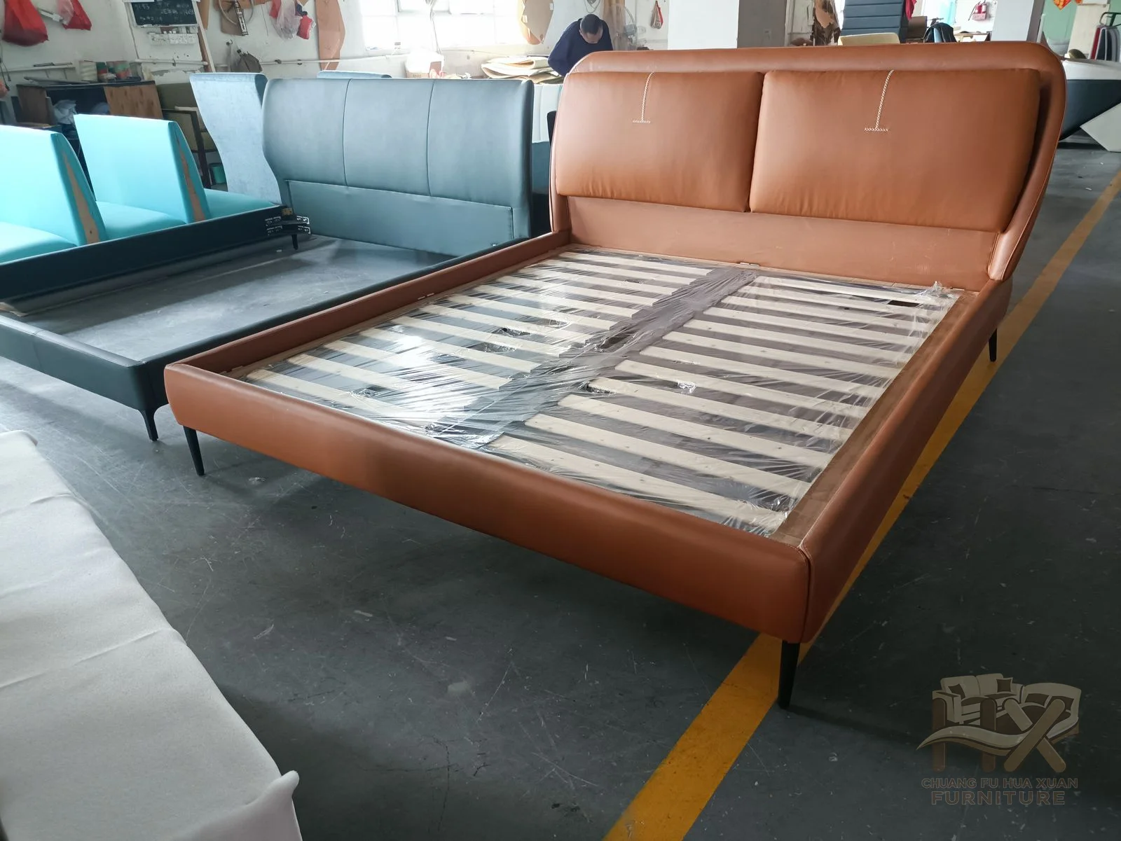 A low bed frame sits below an angled padded headboard, shown in warm brown and muted green finishes.