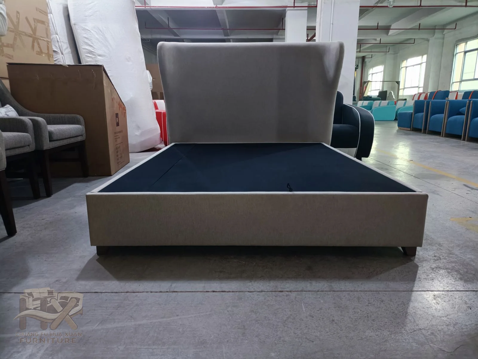 A low grey upholstered base extends below a broad plain headboard that rises behind the mattress area.