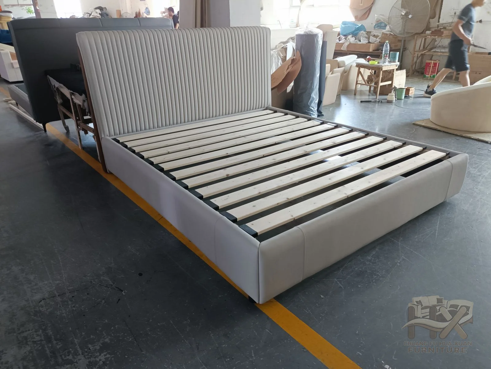 A low bed frame carries a narrow grey padded headboard above a visible slatted support.