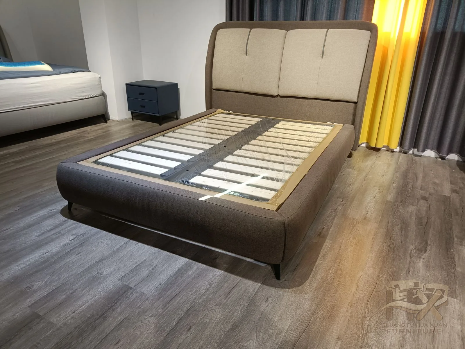 A low upholstered bed frame meets a tall grey padded headboard above visible slats.
