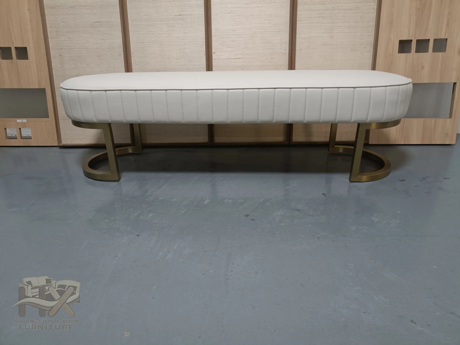A long pale upholstered bench sits over a curved exposed metal-look base with open space beneath.