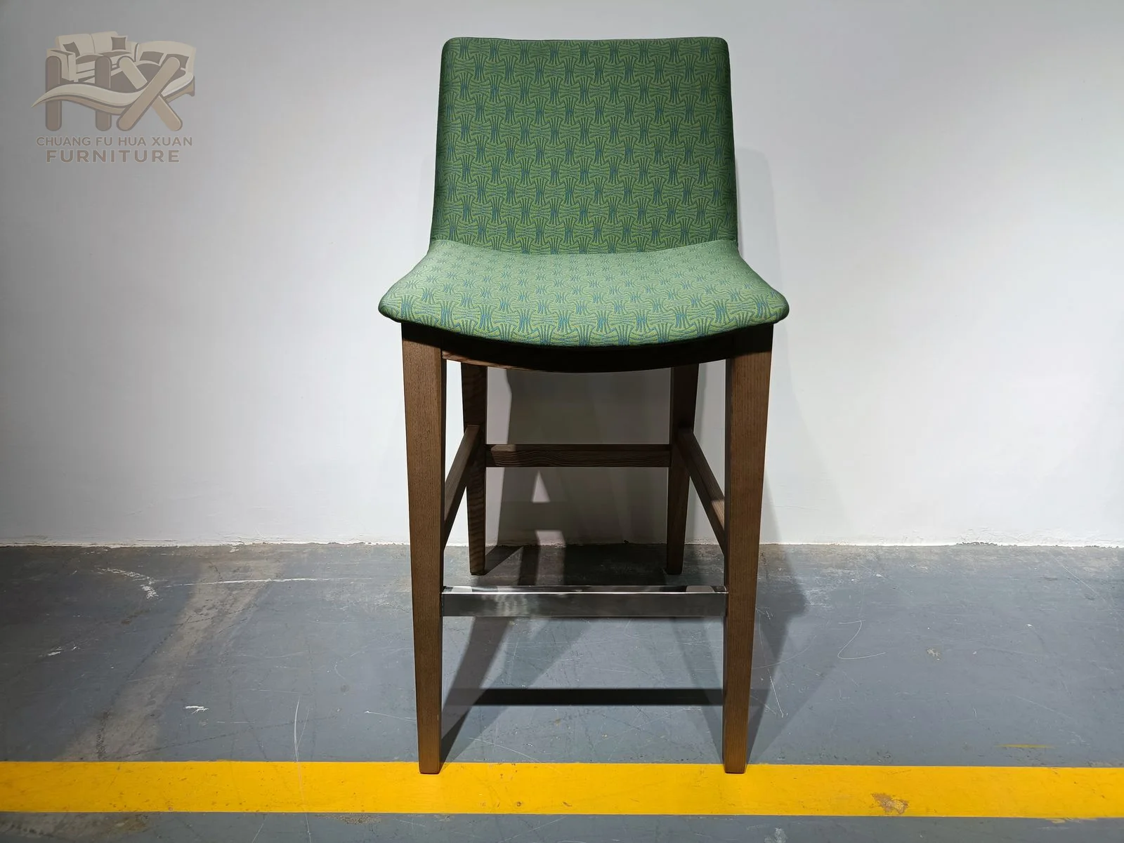 A slim green upholstered back rises above a high seat on a dark open frame with a lower foot rail.