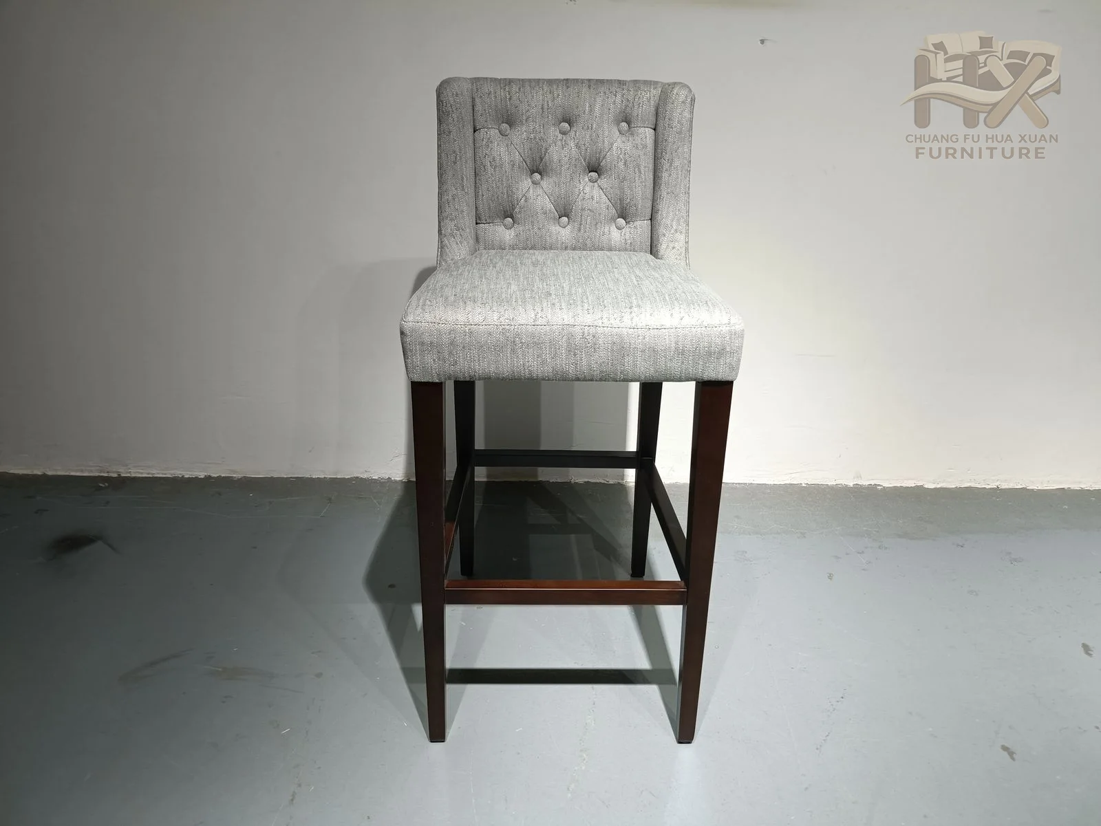 A tall grey back has a buttoned centre above a high narrow seat and open dark footrest frame.