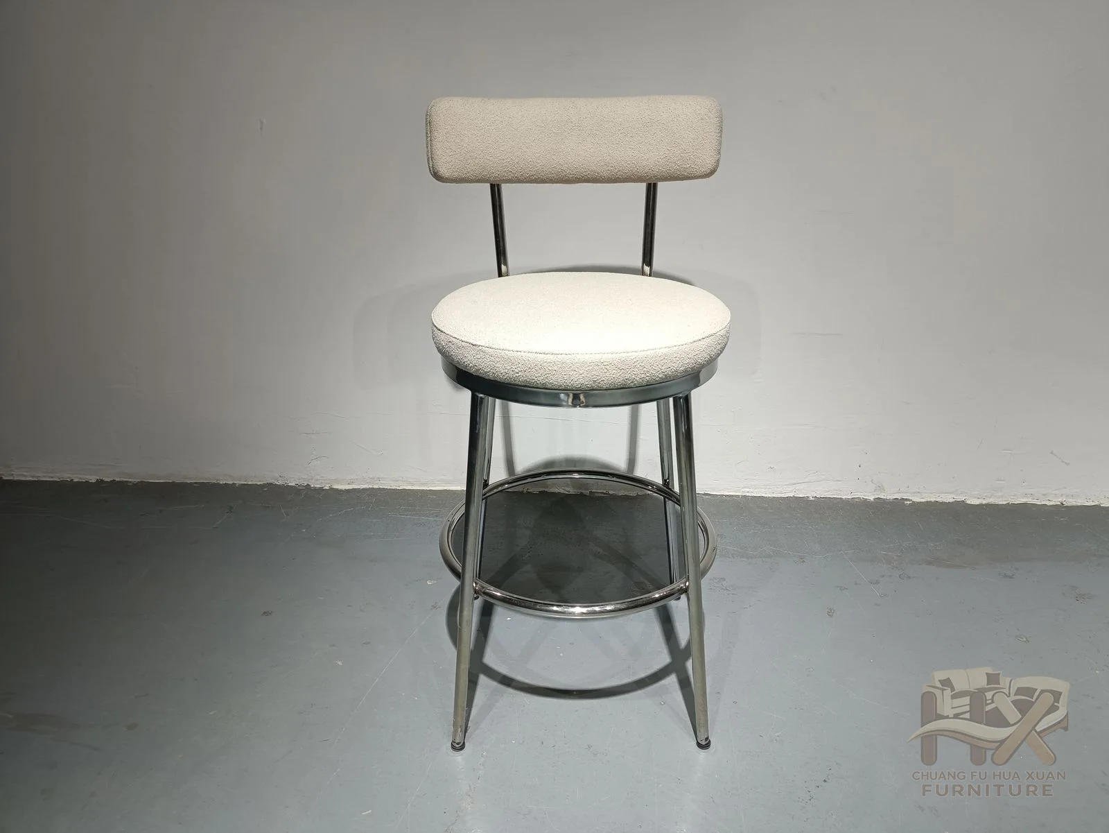 A small circular upholstered seat sits beneath a short back on a thin dark high base with a ring footrest.