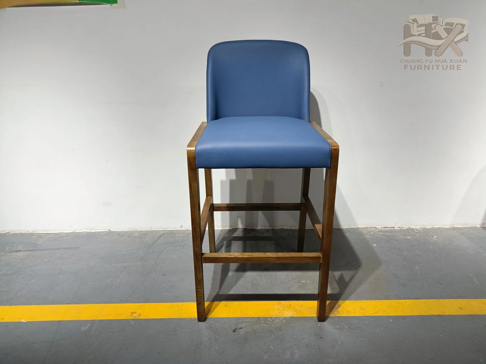 A blue upholstered seat and back rise above a tall dark frame with a foot rail.