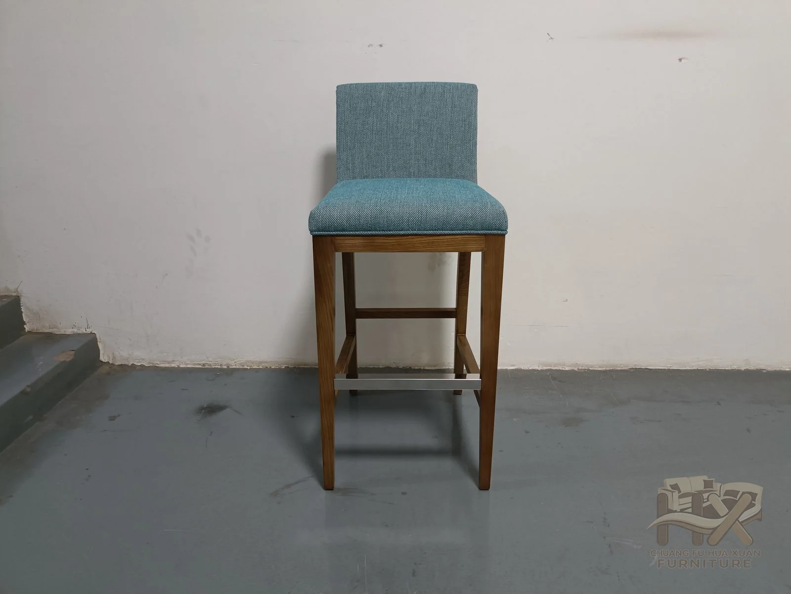A small blue upholstered bar seat stands on tall wood-look legs with a foot rail.