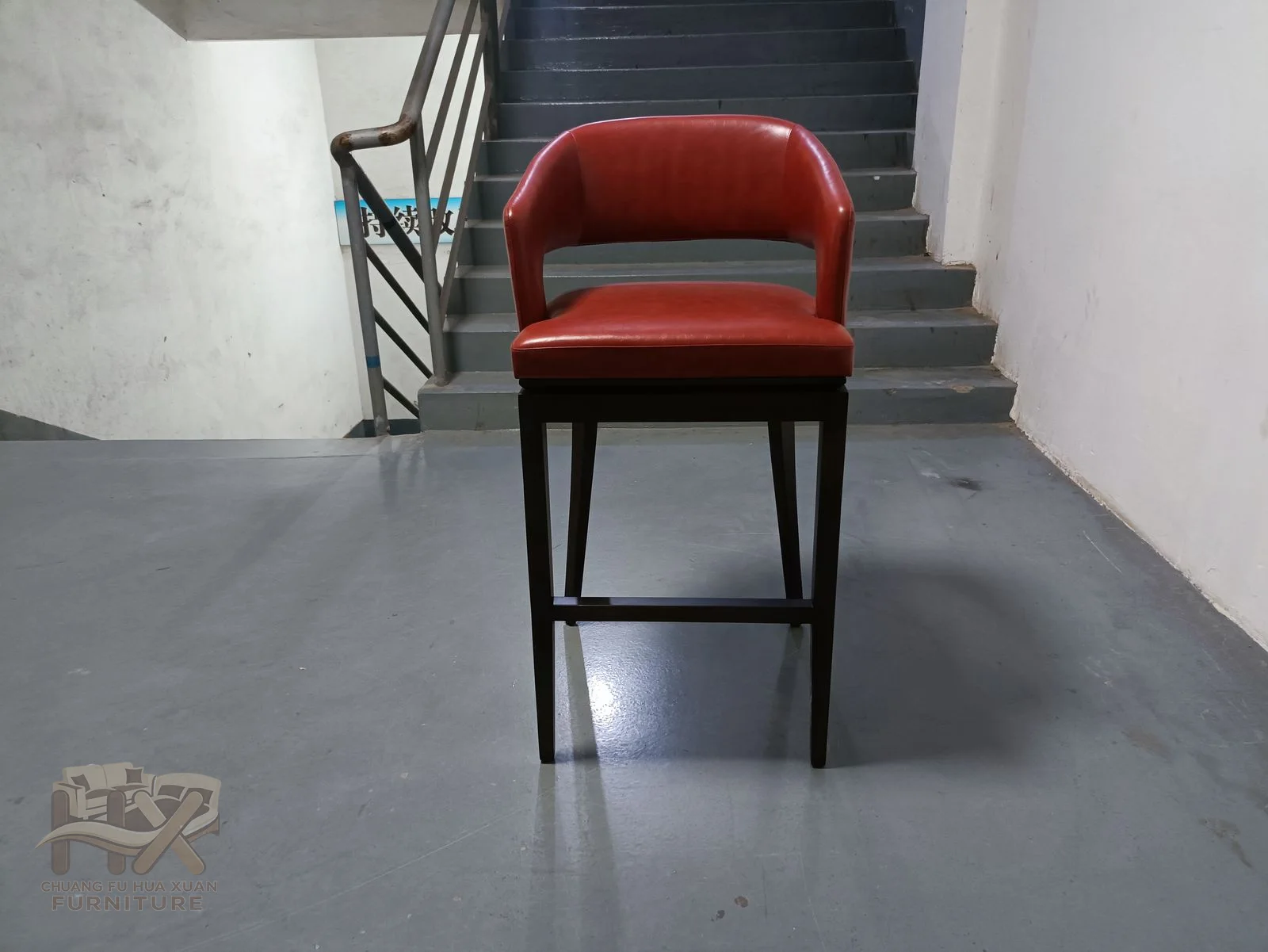 A red padded back and short arms top a high dark bar-chair frame.
