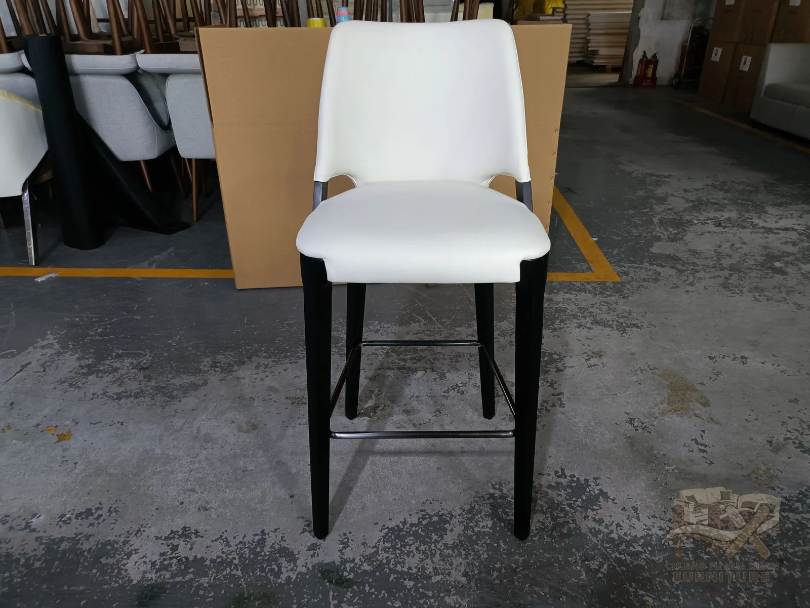 A white padded counter chair has a narrow back above slim dark high legs and a foot rail.