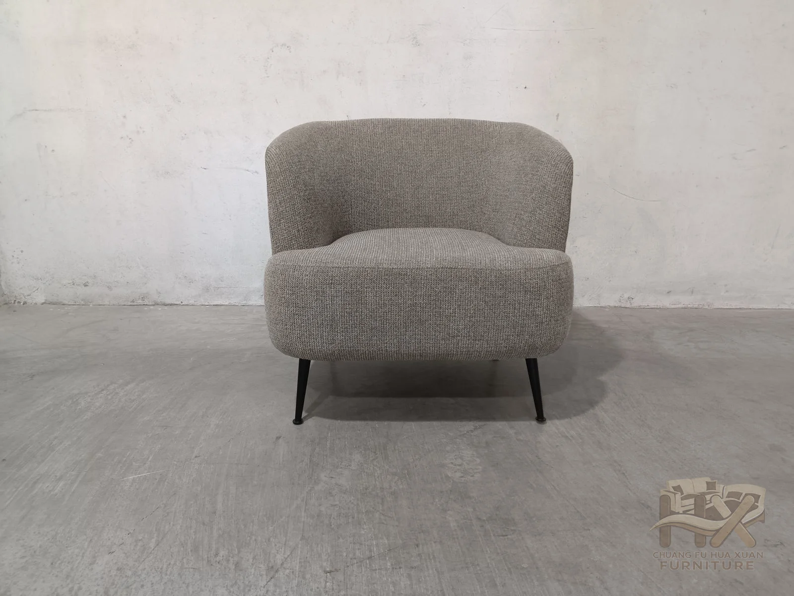 A broad curved back wraps into short arms above a separate seat cushion, while small dark feet leave the body close to the floor.