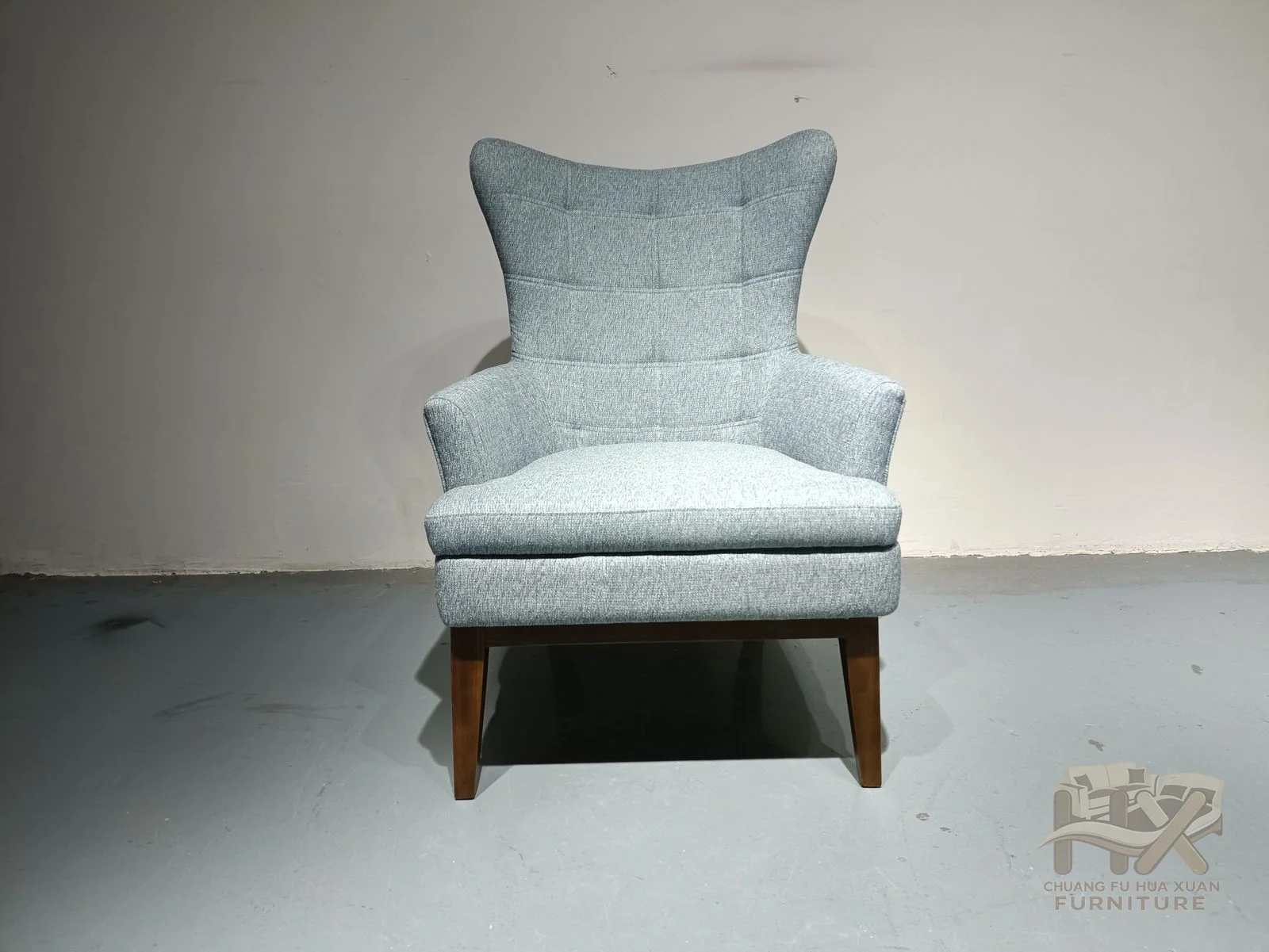 The chair has a high winged back, a loose seat cushion and short exposed legs beneath its pale blue upholstery.