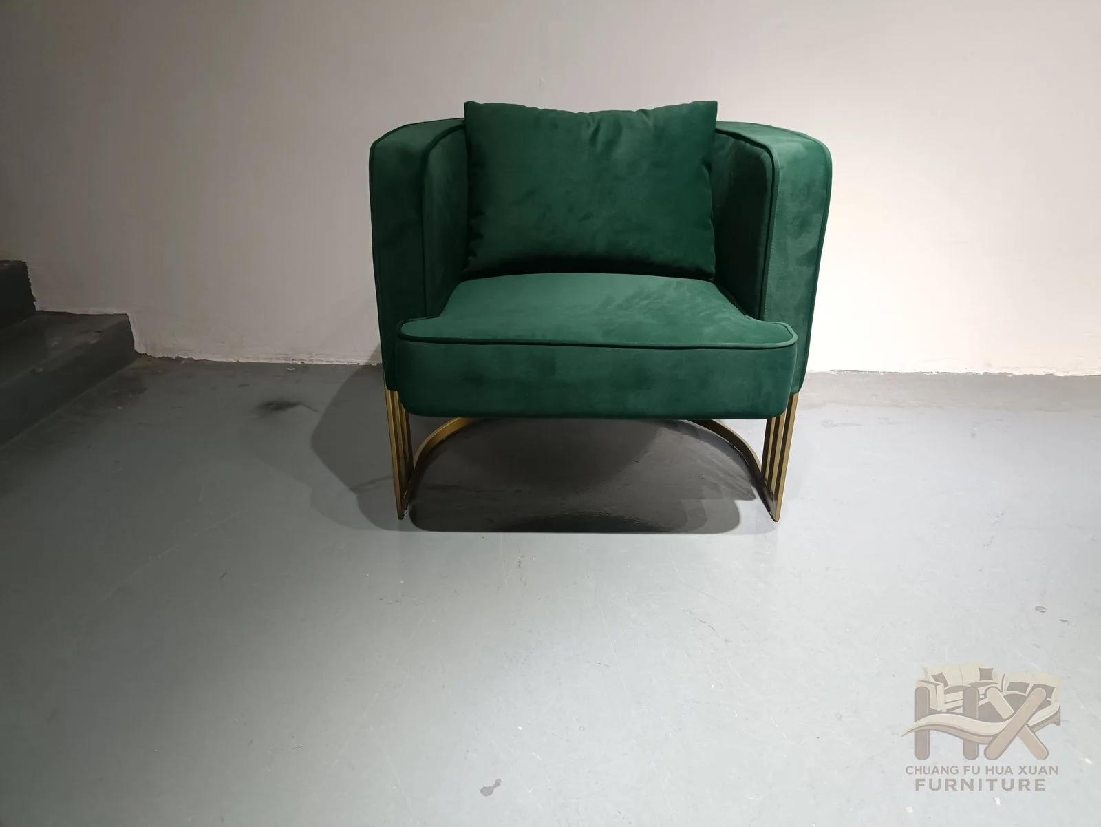 Rounded emerald upholstery is framed by several bright metal-look rails that travel around the outer arms and down to a circular base.