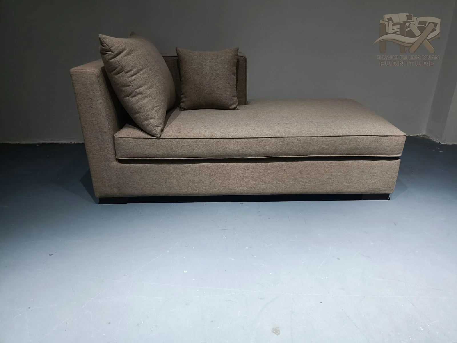 A long upholstered seat extends beyond a low-sided back enclosure, with two loose pillows forming the back support.