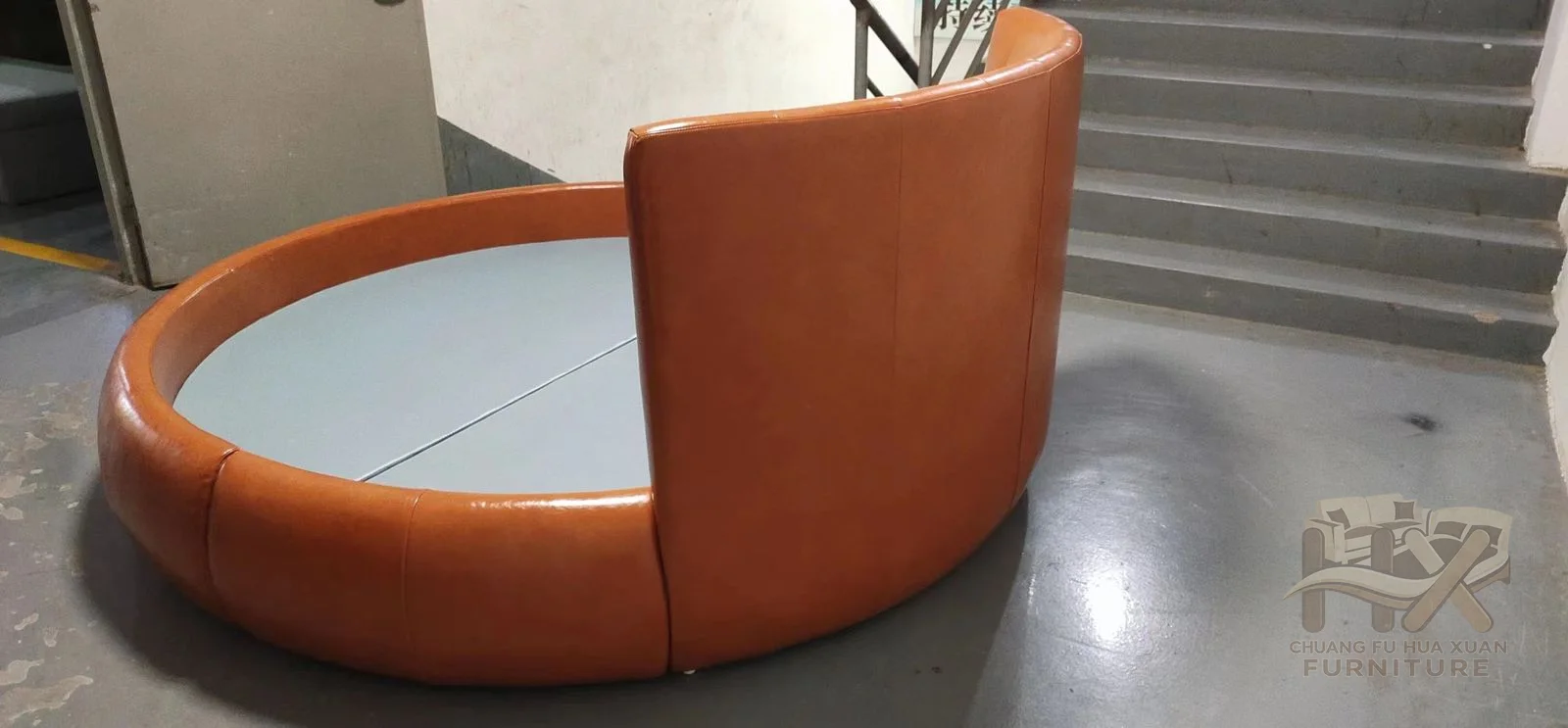 A circular upholstered platform wraps into a partial curved back, with tan vertical channels rising at one side.