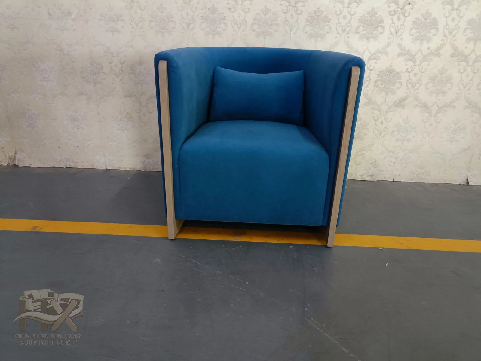 A square blue back surrounds a compact seat, with narrow metallic edges outlining the upholstered sides.