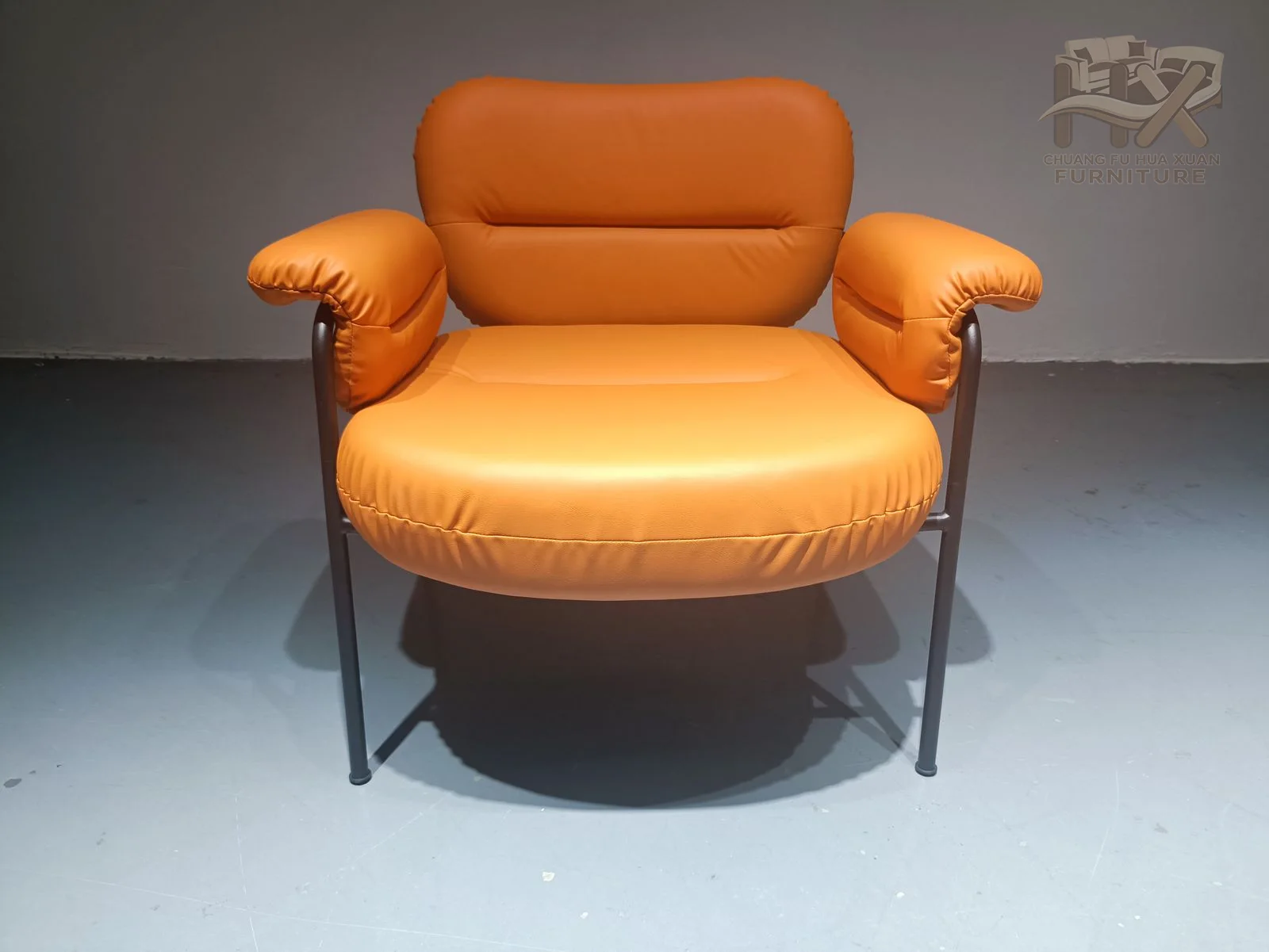 A plump orange seat sits inside an airy dark frame, with a short back cushion and rounded arm pads.