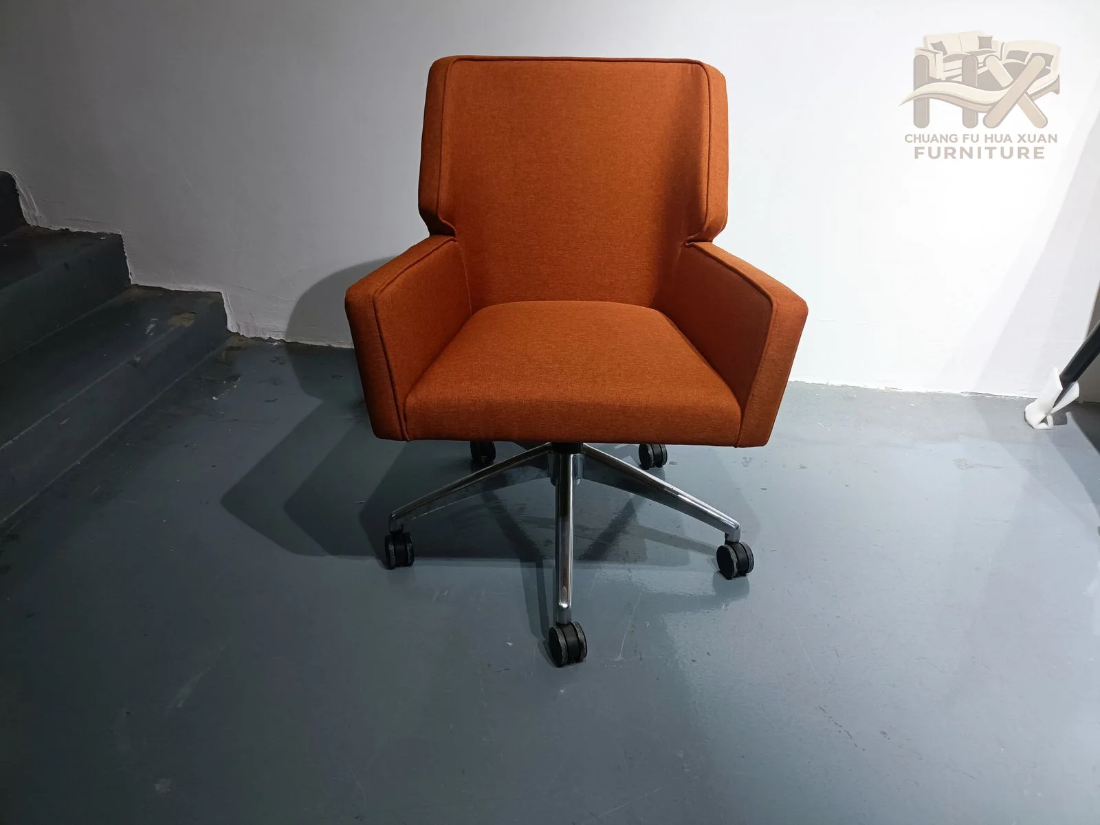 A tall orange upholstered back and compact seat are supported by a wheeled swivel base.