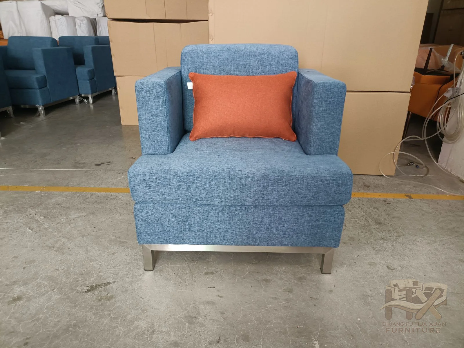 A broad square blue back meets wide low arms, with a small warm-toned accent cushion on the seat.