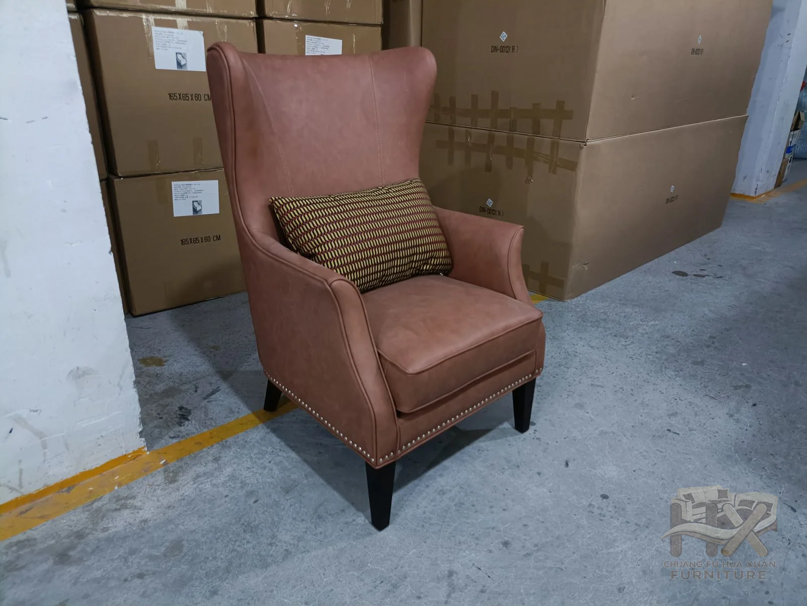 The brown chair has a tall winged back and a loose seat cushion above dark tapered legs.