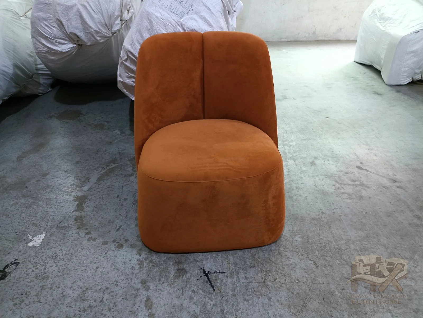 A rust-coloured rounded seat rises into a short padded back, with no exposed arms interrupting the outline.