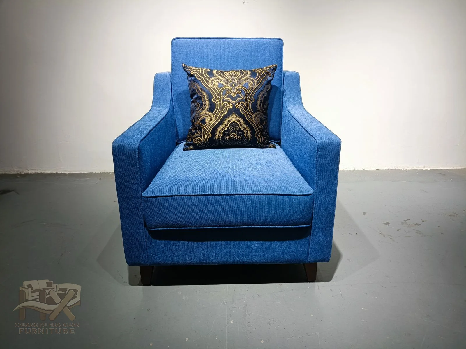 A bright blue high back rises above narrow arms and a compact cushion, with a patterned loose pillow at the centre.