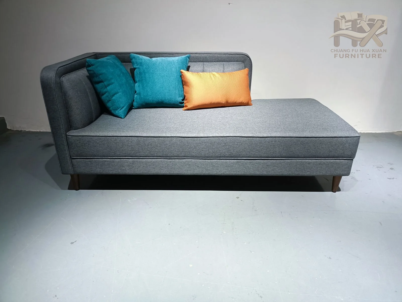 A long grey chaise seat meets a low back holding turquoise and ochre pillows above an upholstered base.