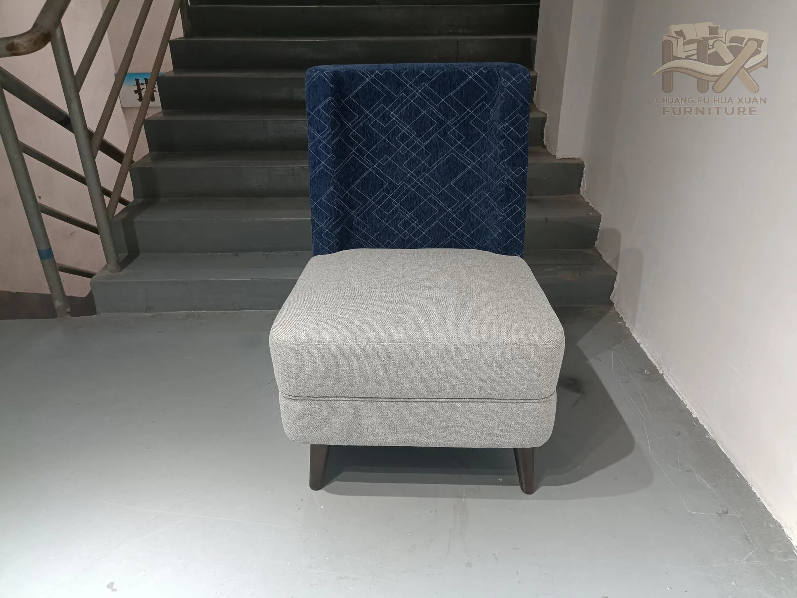 A long pale seat projects from a tall deep-blue upholstered back panel without a second enclosing arm.