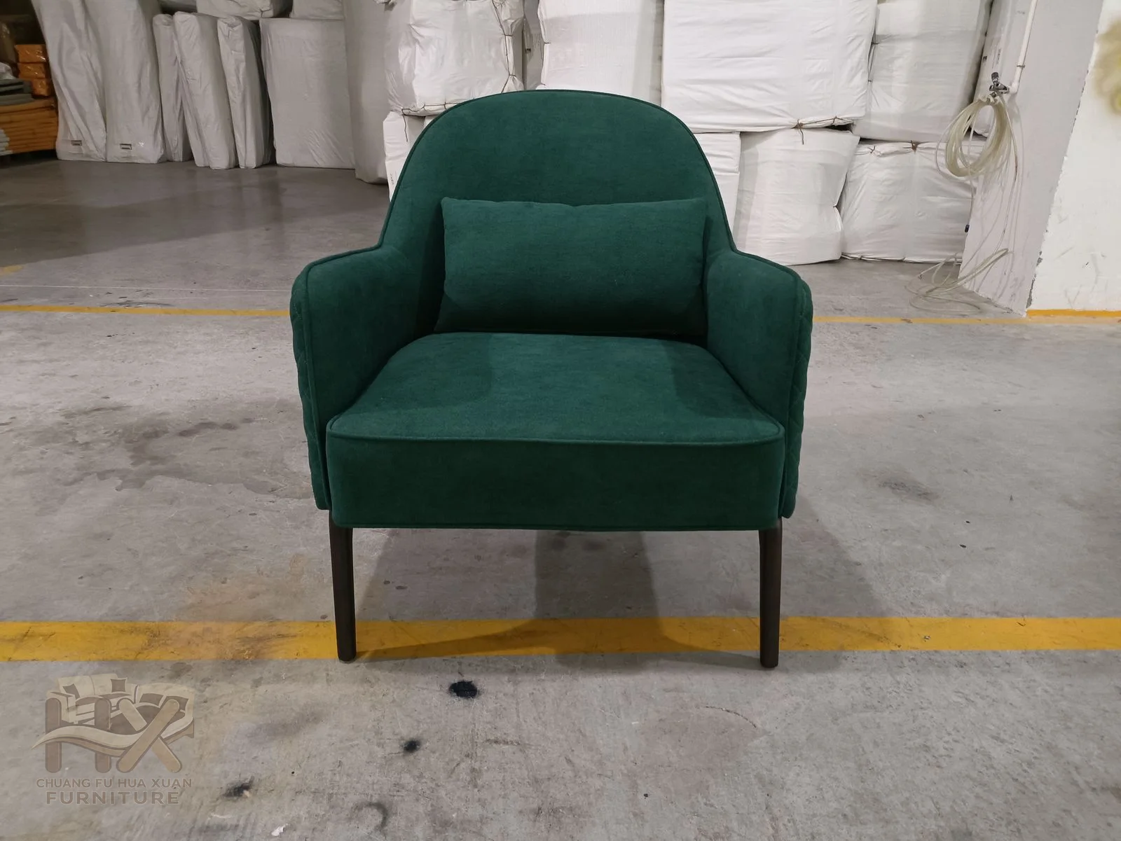 A dark green back curves into rounded arms above a small seat and slender warm metal-look legs.