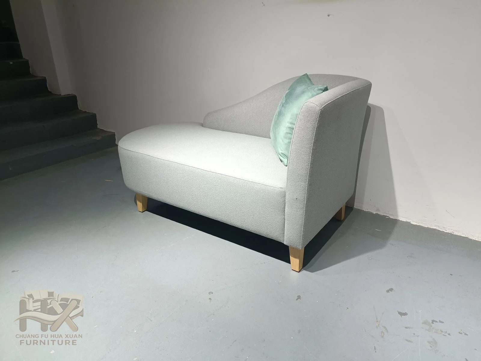 A white chaise has one long side panel and a low inclined seat with a small contrasting cushion.
