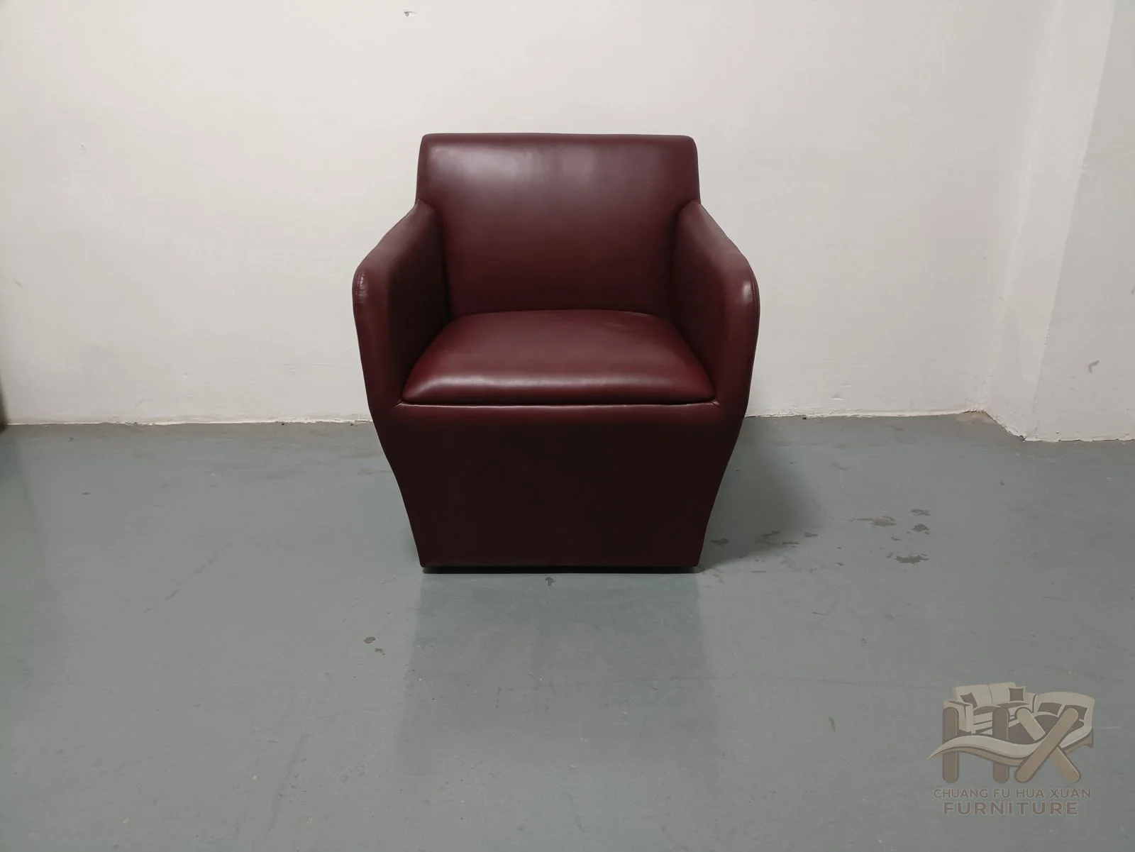 A small burgundy chair rounds its back and arms around one low seat with no visible legs.