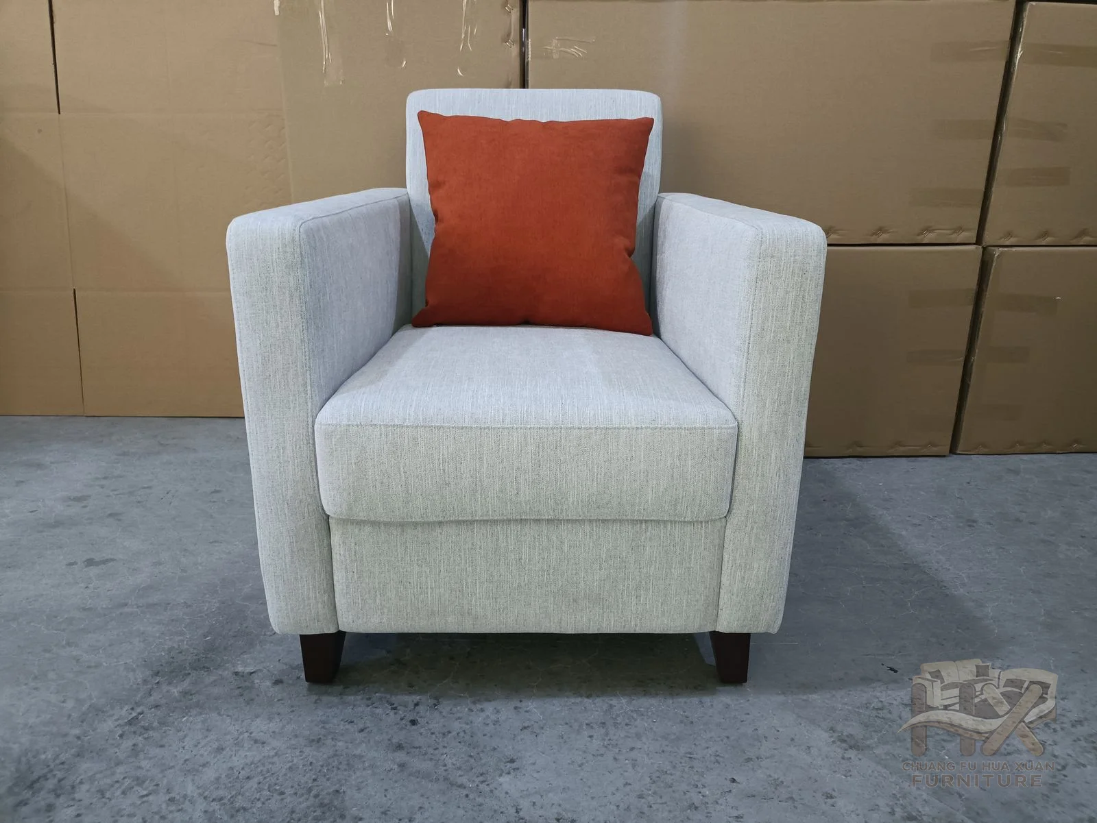 A square white chair carries a single rust-red loose cushion within its straight arms.