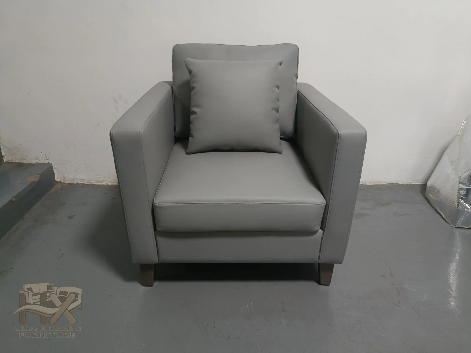A grey club chair has a high padded back and upright square arms above a compact base.