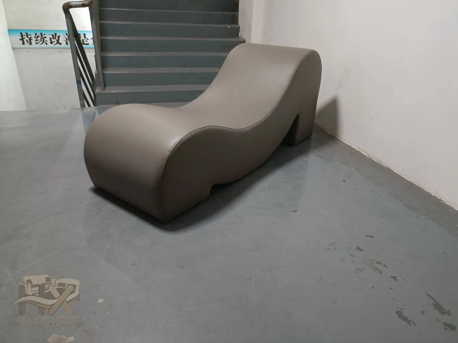 A taupe chaise undulates from a raised back to a long reclining seat without projecting arms.