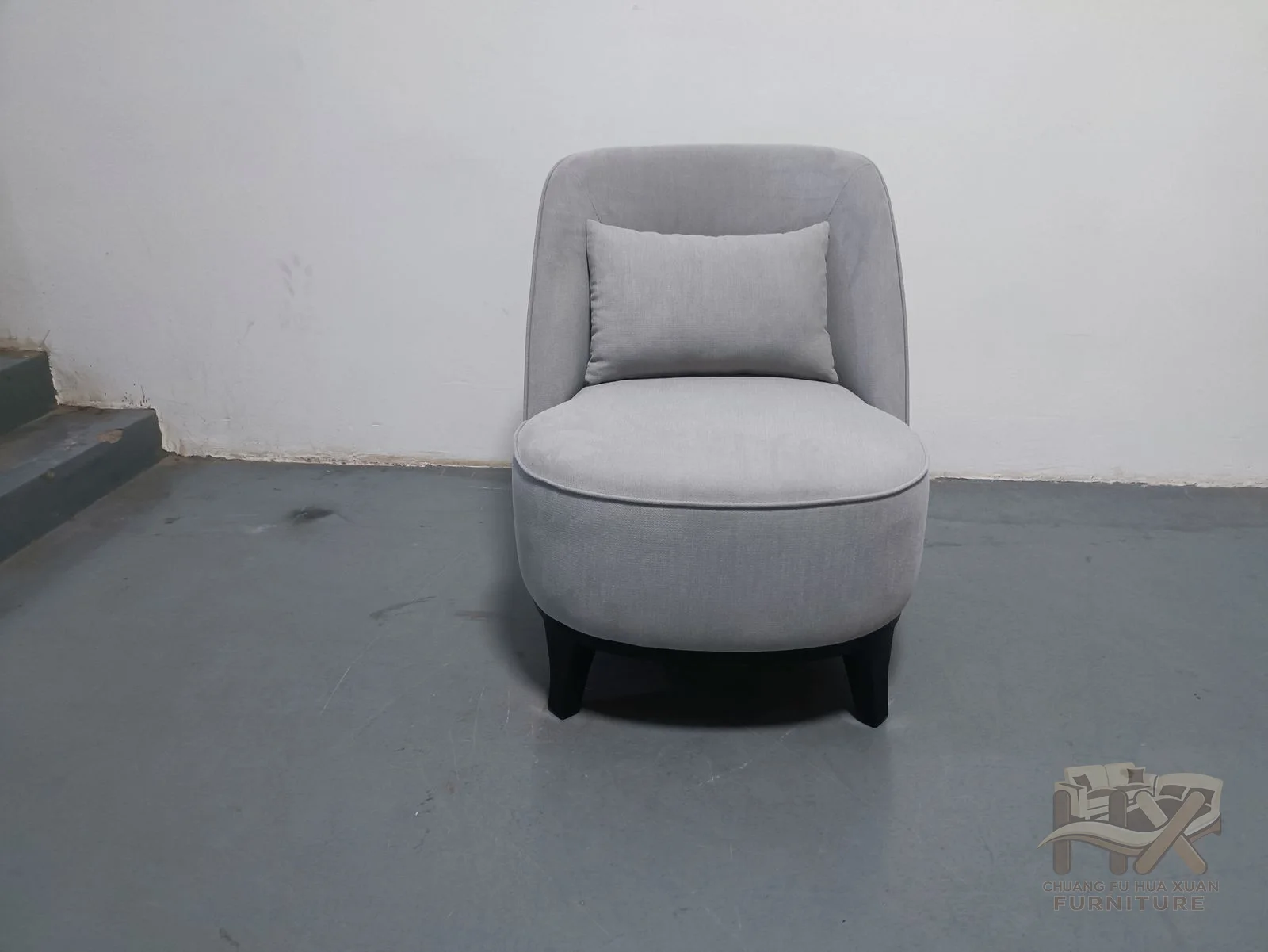 A pale grey chair rounds its arms and back around a broad individual seat on a low base.