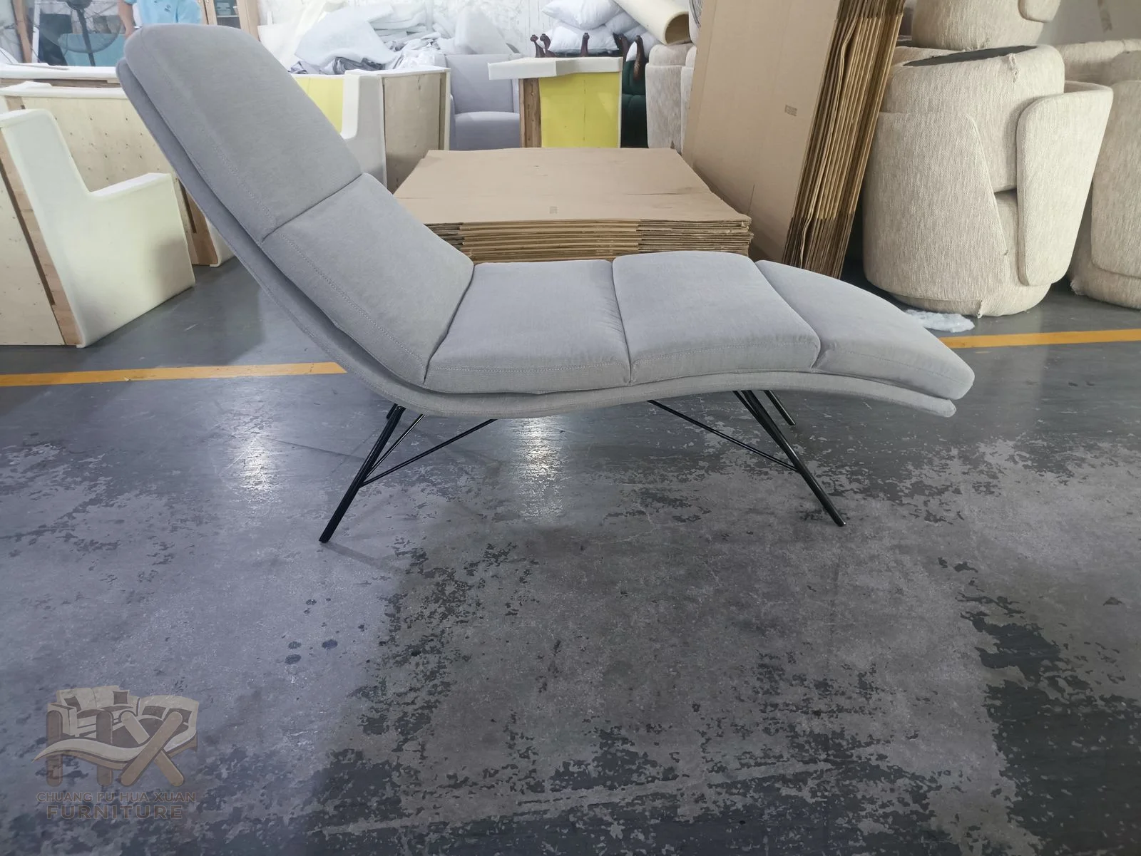 A long grey padded chaise reclines over a slender exposed metal-look frame.