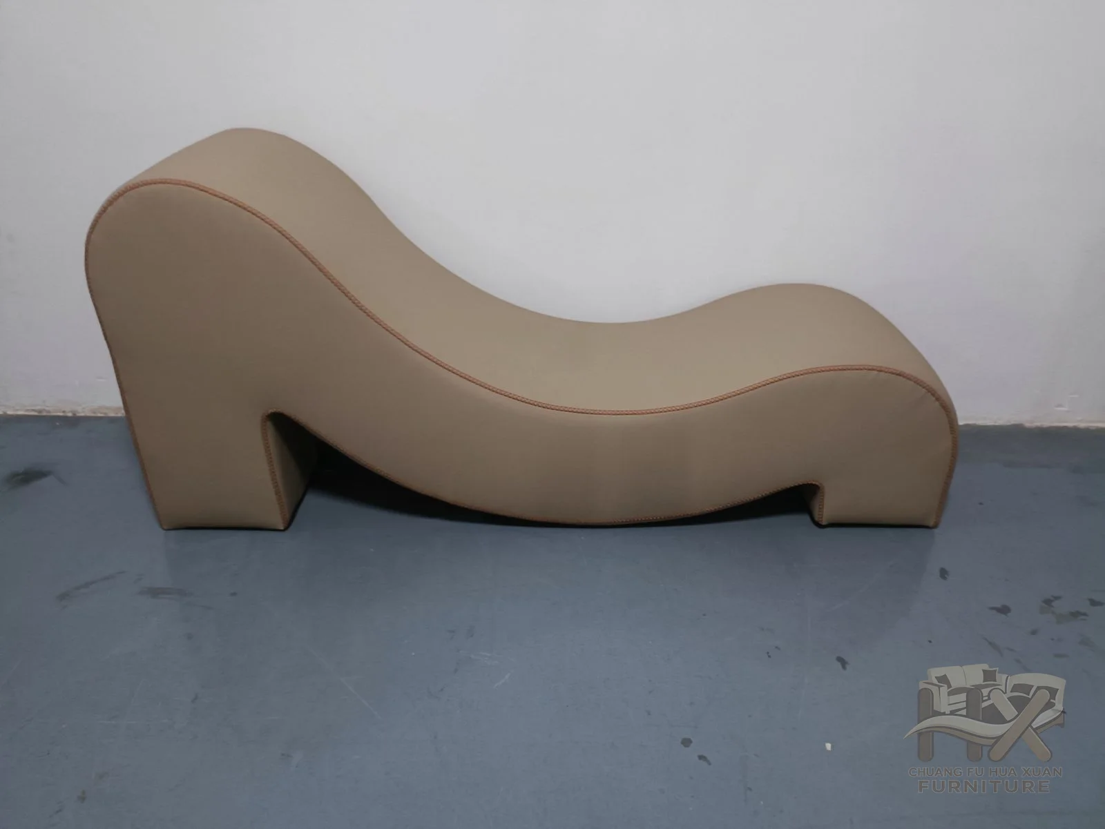 A taupe upholstered chaise rises and dips in one continuous reclining wave.
