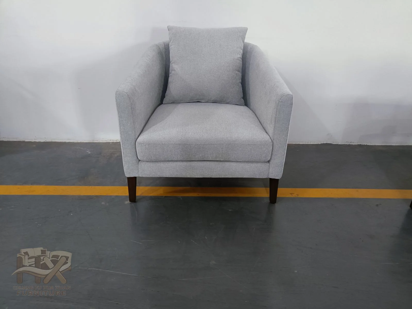 A grey club chair has a rounded back and short arms above slim dark feet.