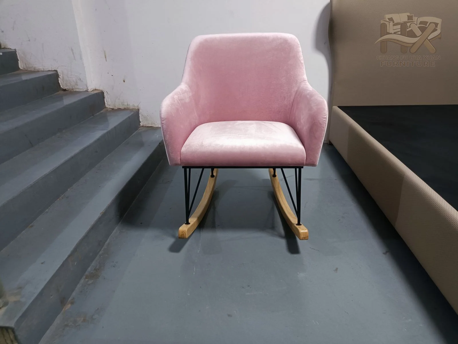 A pink upholstered shell and broad seat rest on an exposed rocking base.