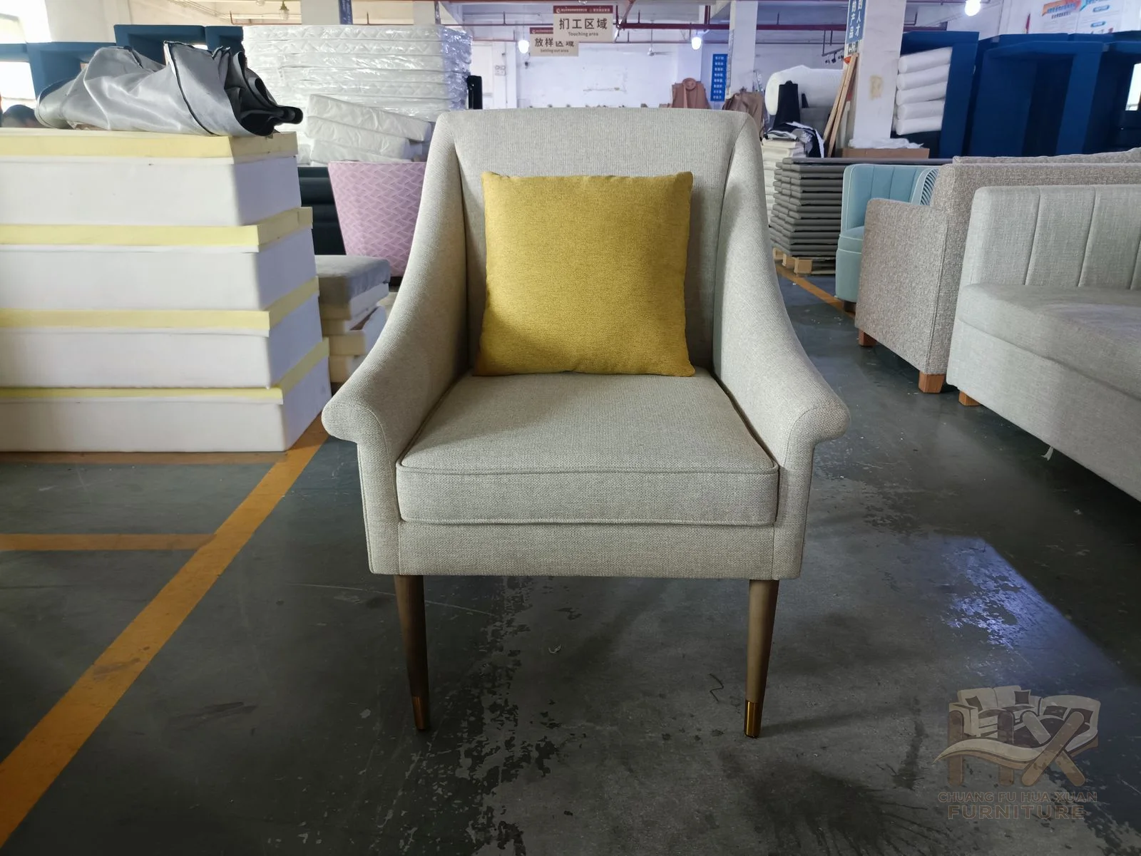 A grey lounge chair has a broad seat and curved short arms with yellow loose cushions.