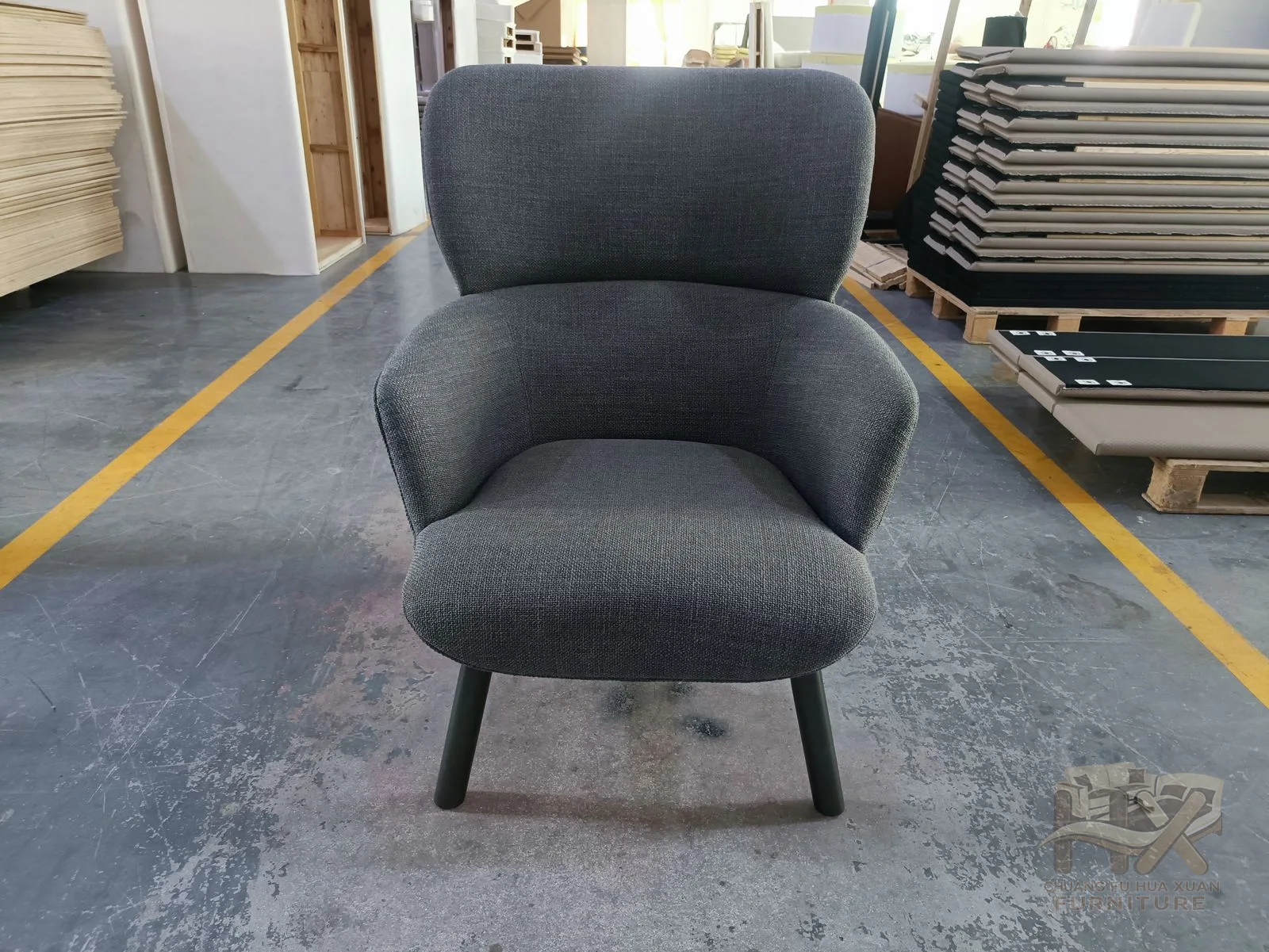 A grey individual chair has a high padded back and extended foot support on a low base.