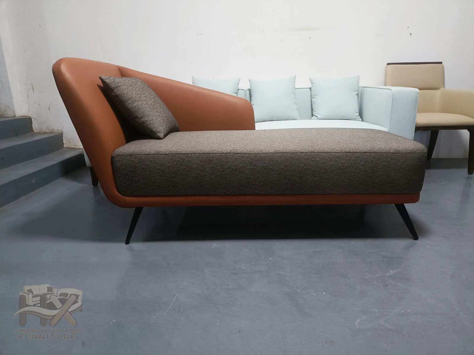 A low taupe chaise carries a rust-coloured sloping back above a long reclining seat.