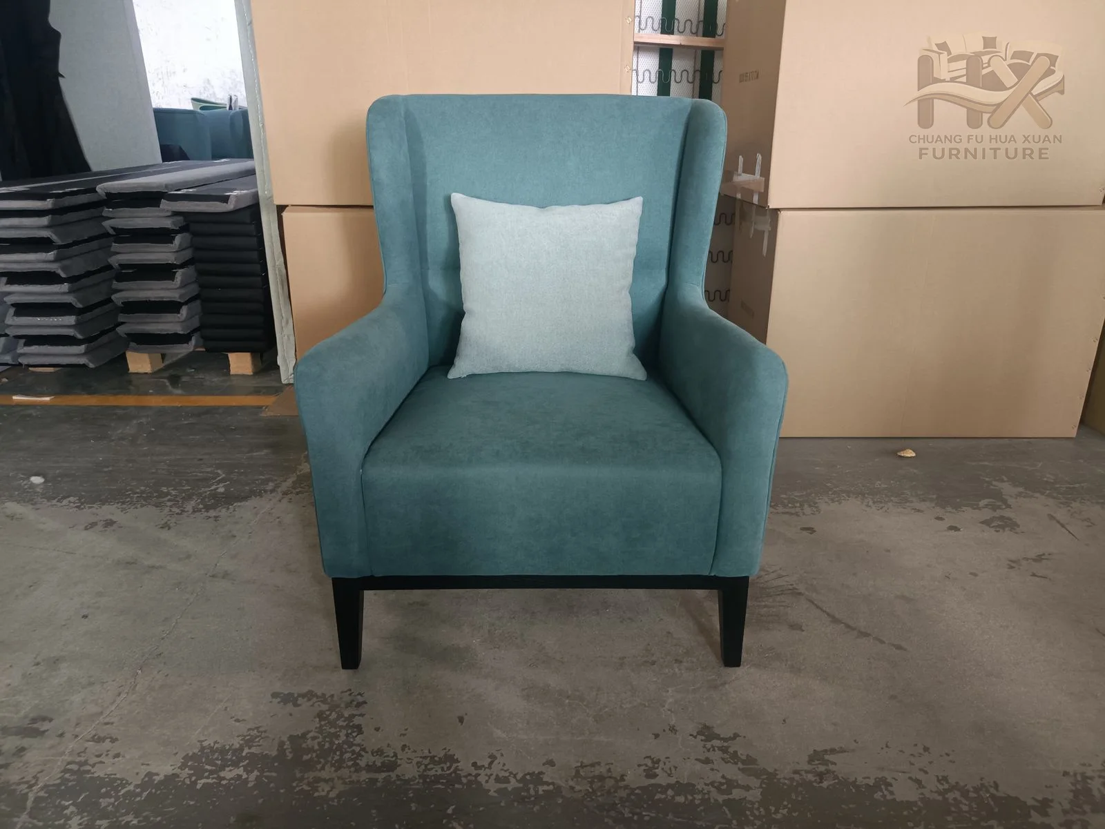 A teal accent chair rises into a high winged back above a compact padded seat.