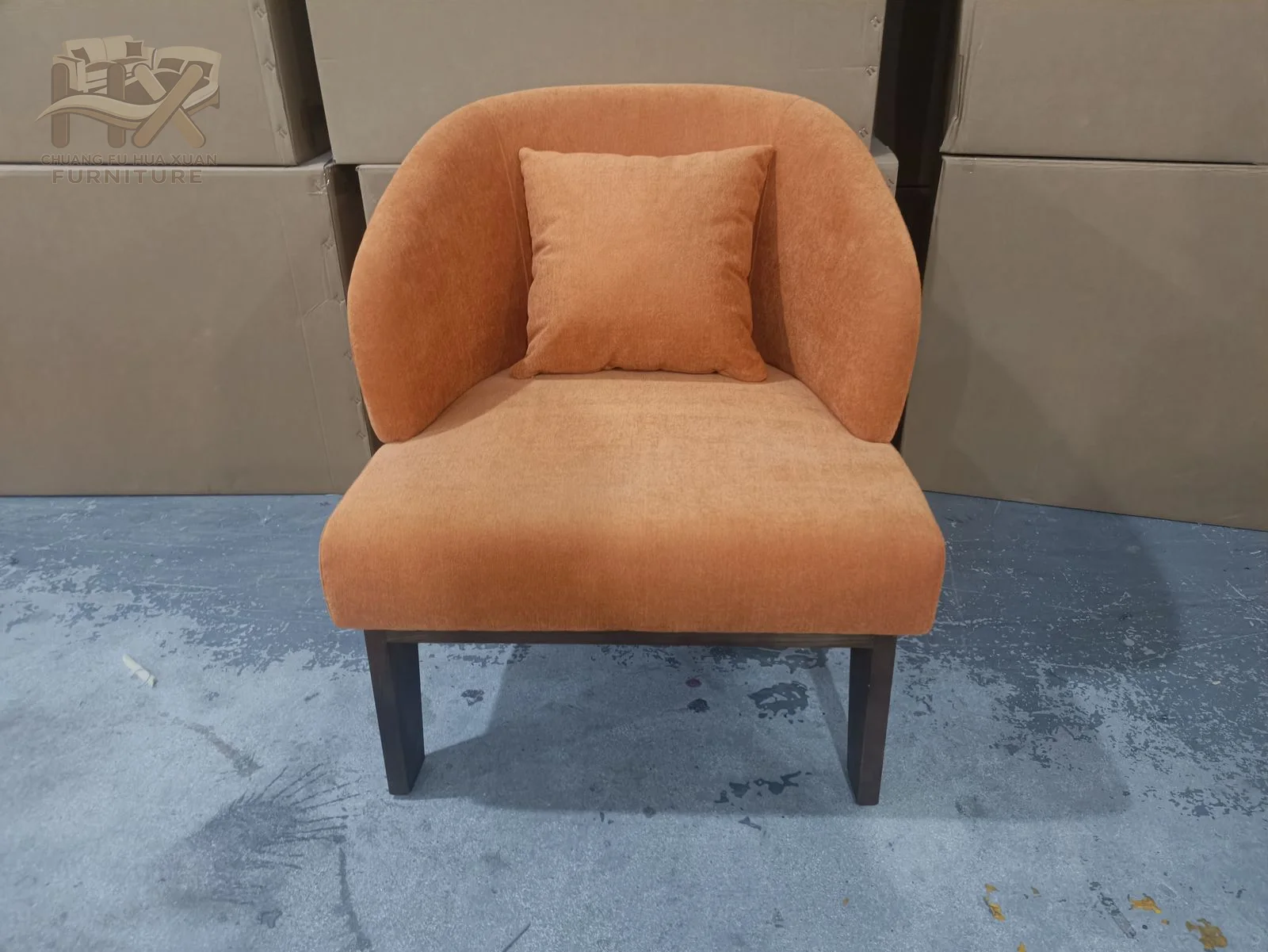 A rust-coloured chair has a high softly winged back and rounded compact seat on dark legs.
