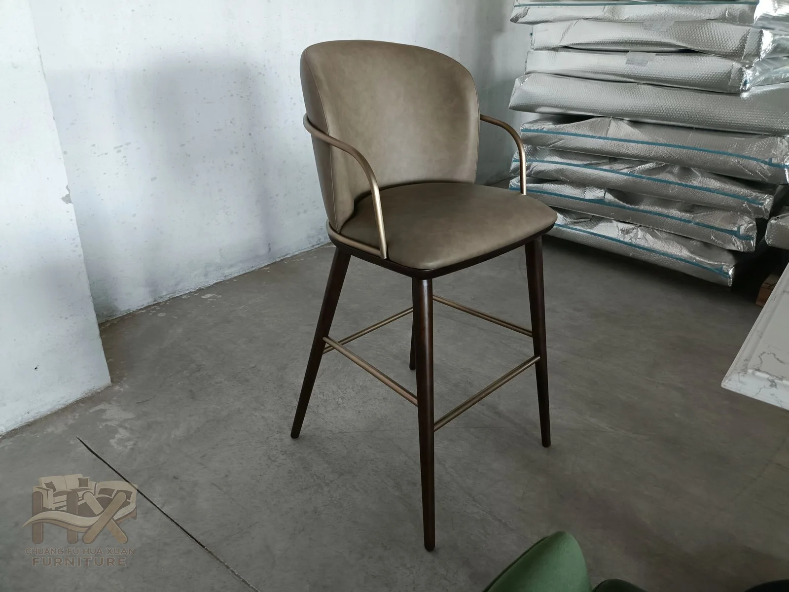 A muted taupe upholstered back and seat are framed by narrow dark metal-look arms and long legs.