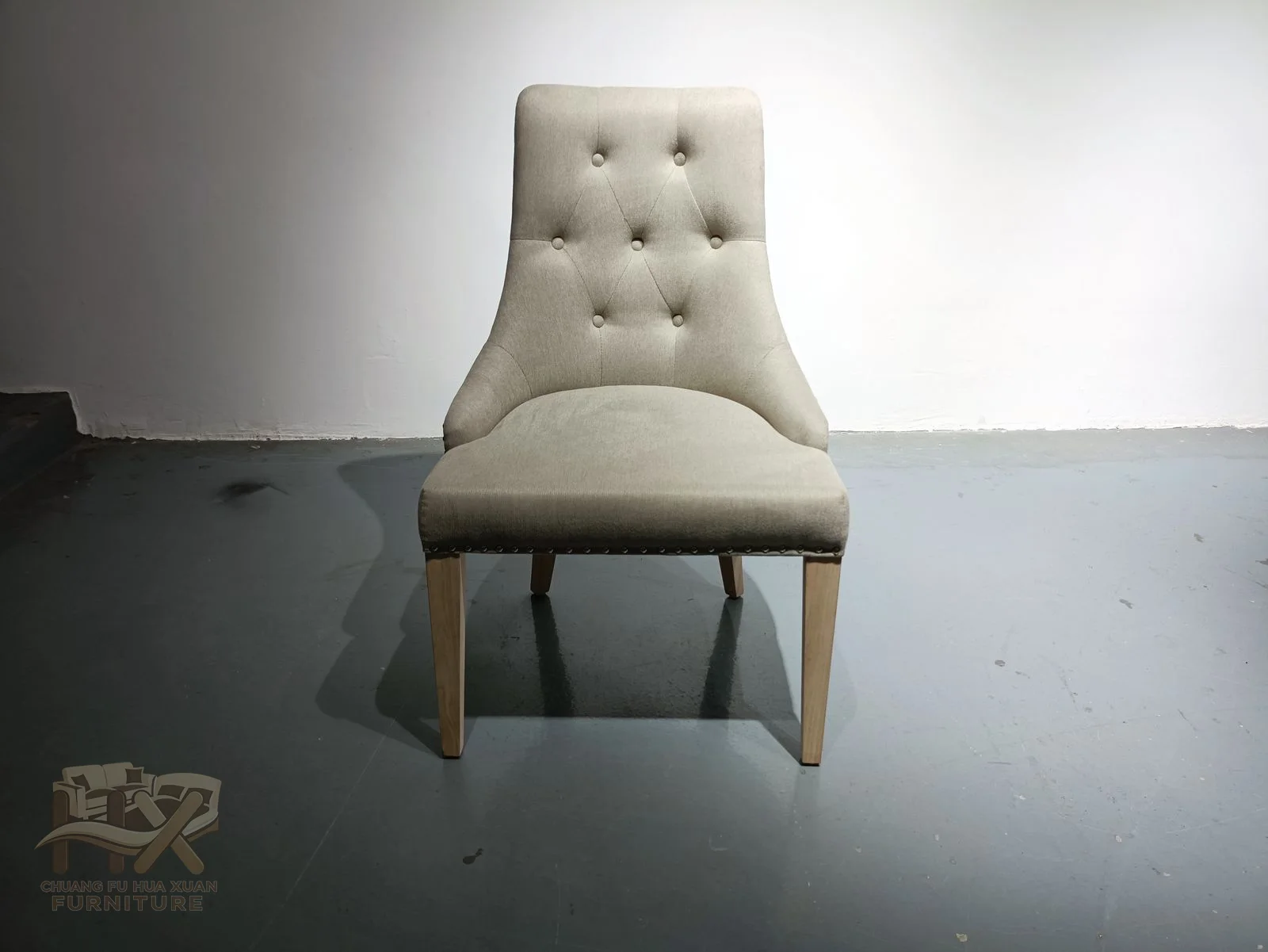 A tall ivory chair back carries a neat button pattern above a slim padded seat and dark tapered legs.