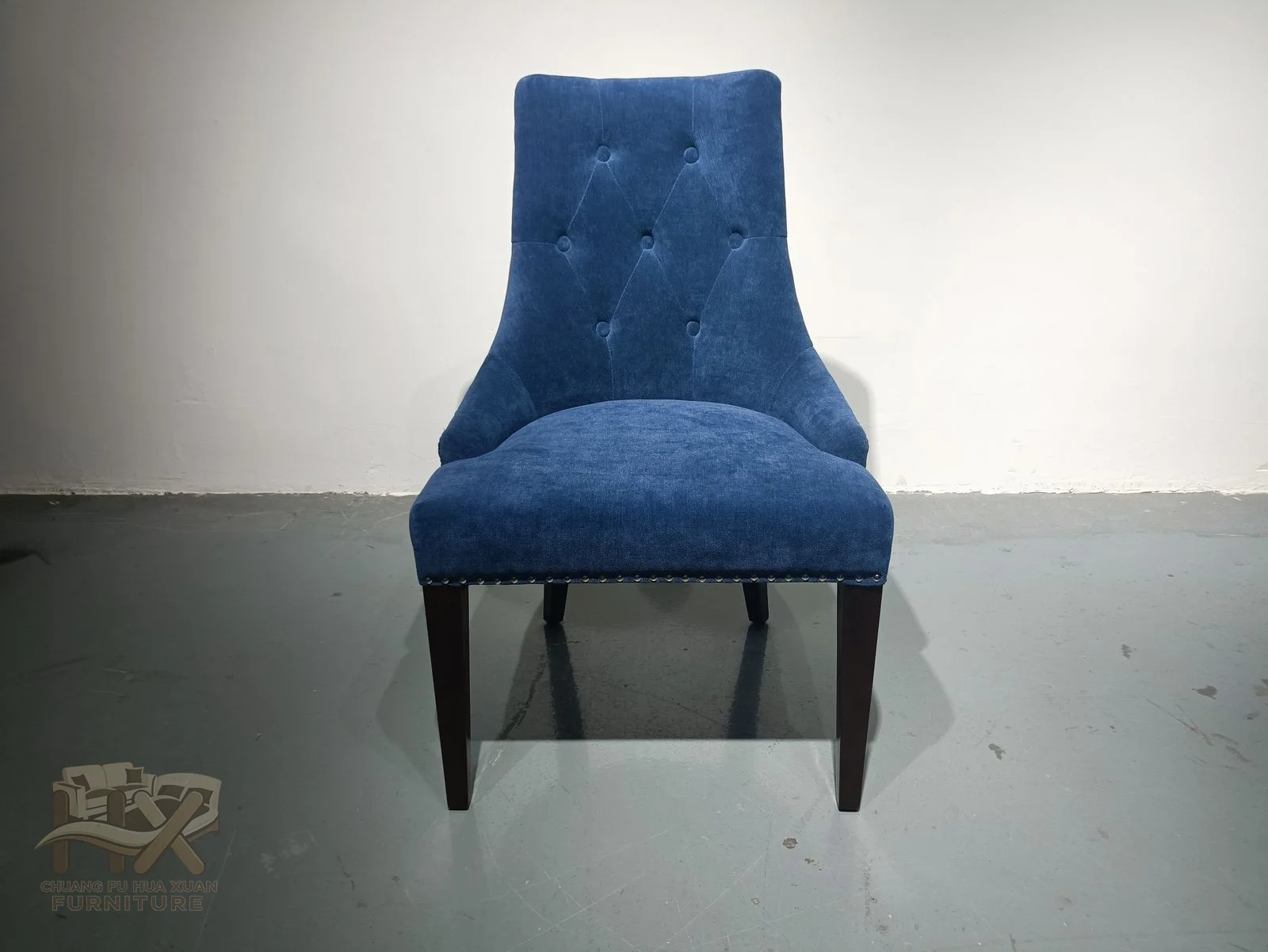 A blue upholstered dining chair rises into a tall tapered back above a slim seat and dark legs.