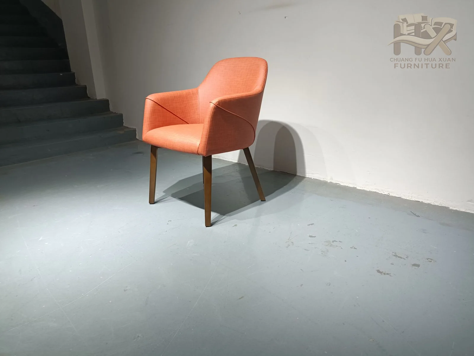 A coral upholstered back bends toward short arms above a compact seat and slim dark legs.