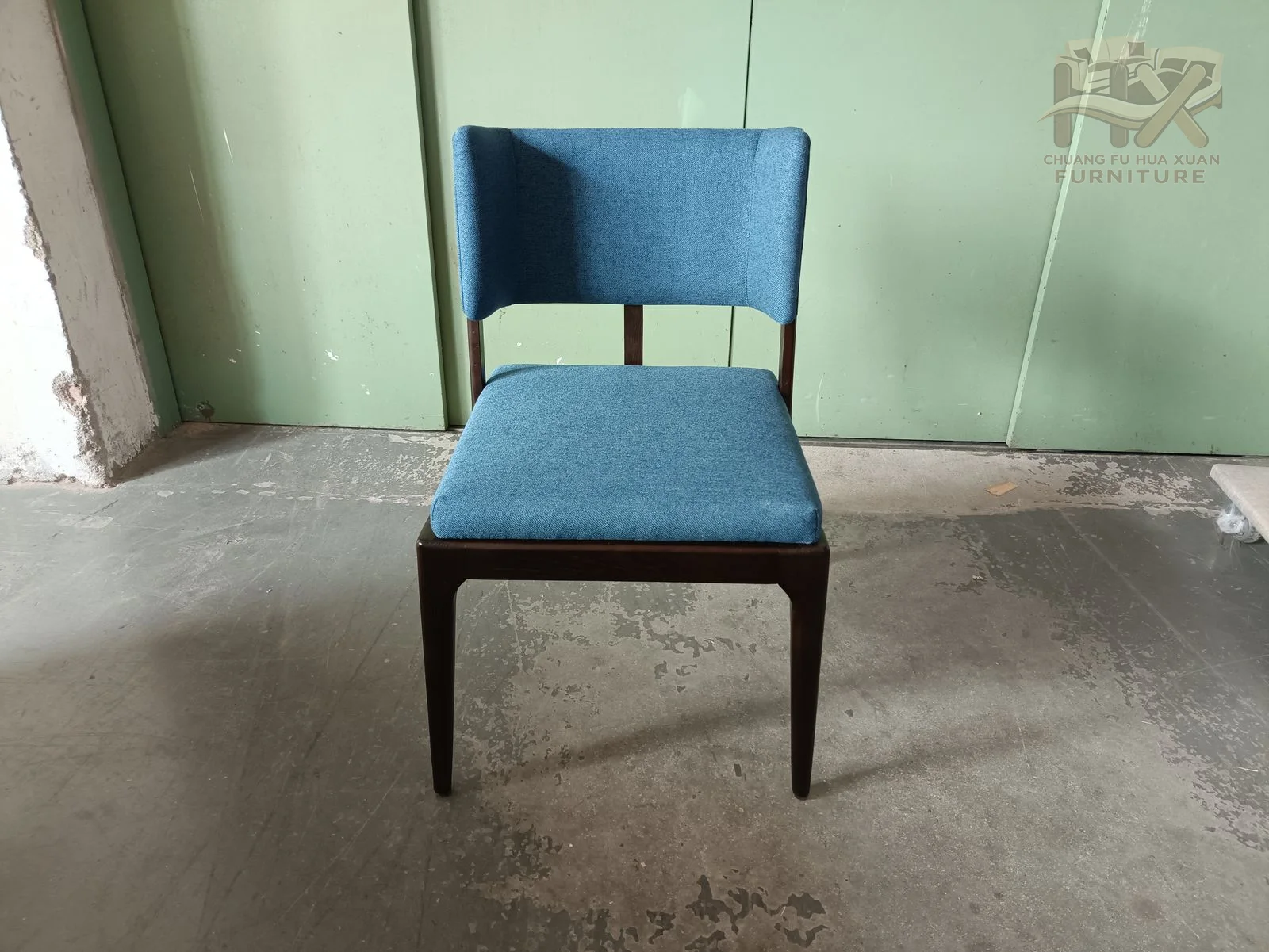 A blue upholstered straight back meets a narrow seat over slim dark tapered legs.
