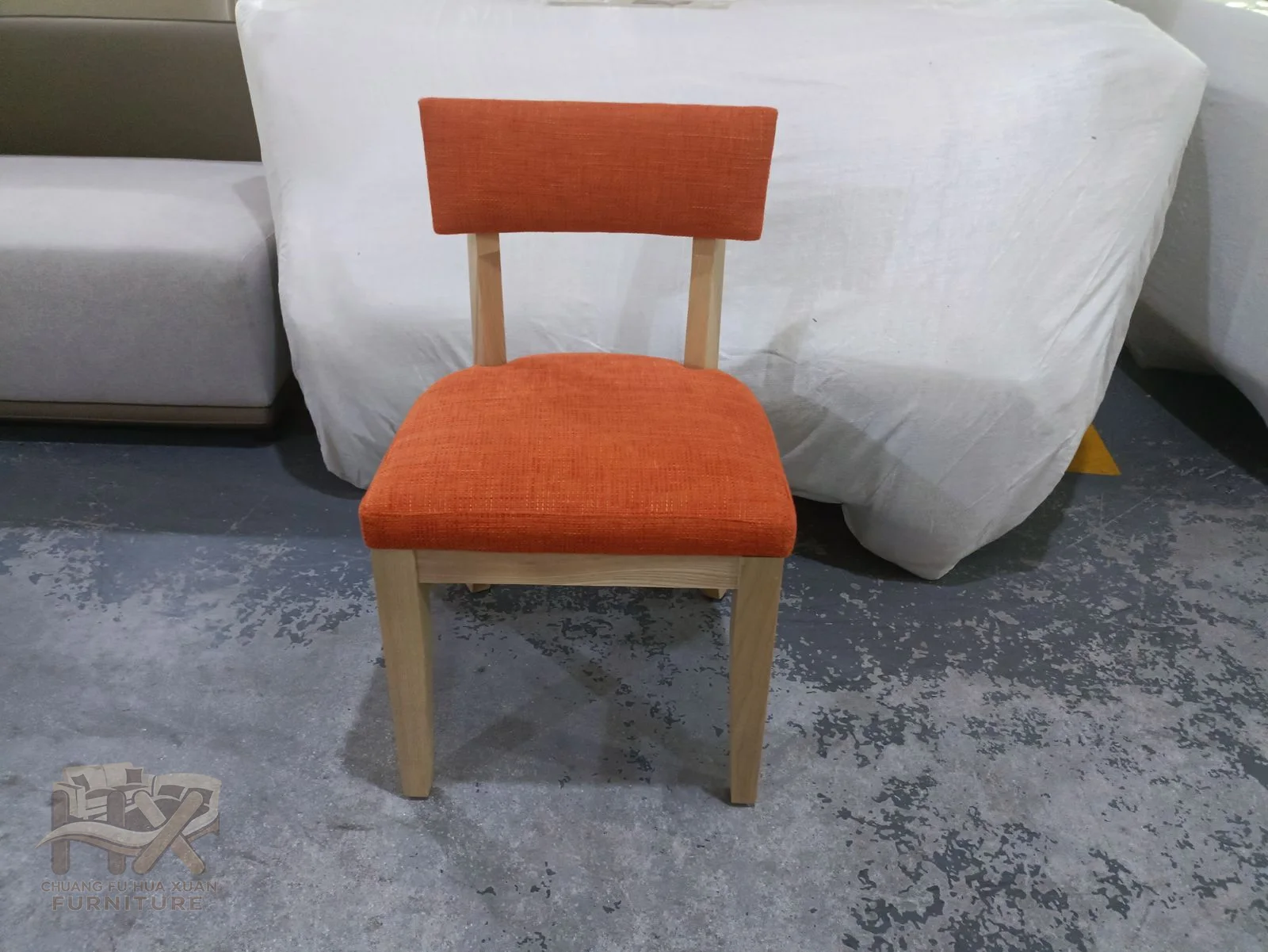A warm orange dining chair places a shaped upholstered back on slim dark legs.