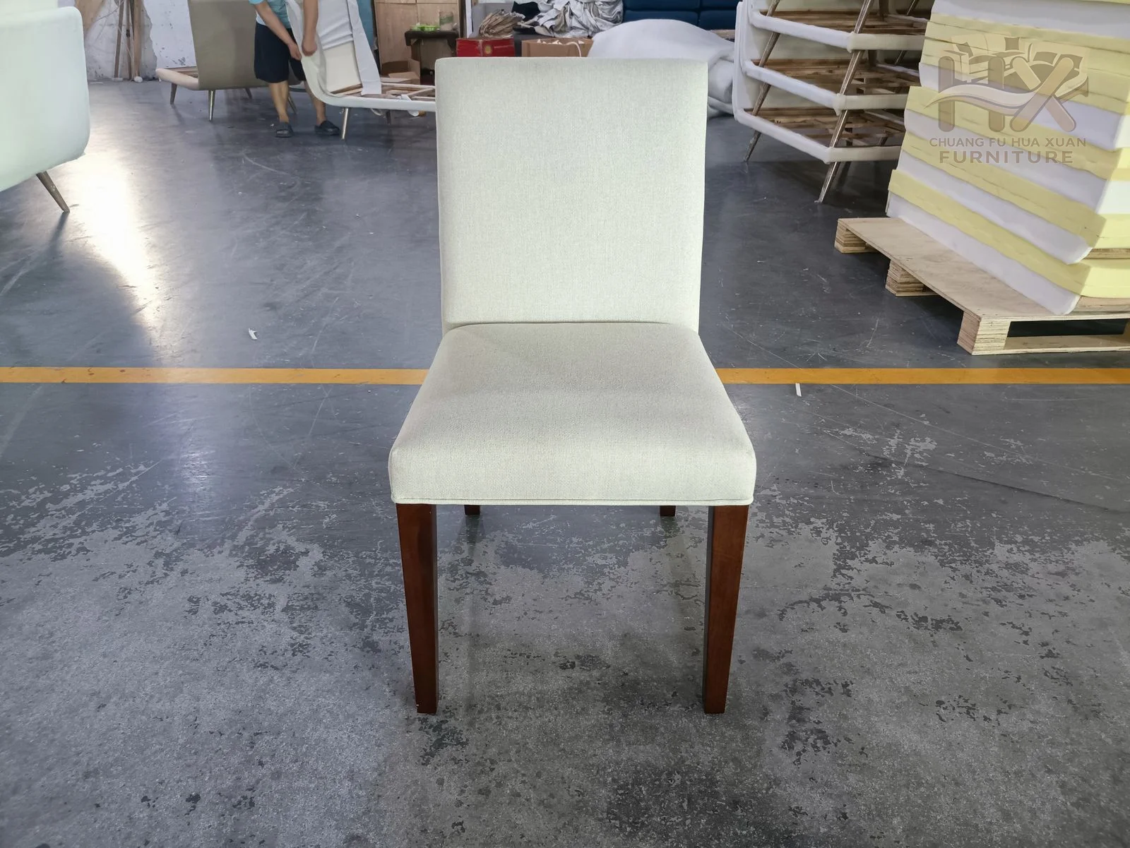 A white upholstered dining chair has a straight upright back and slim pale legs.