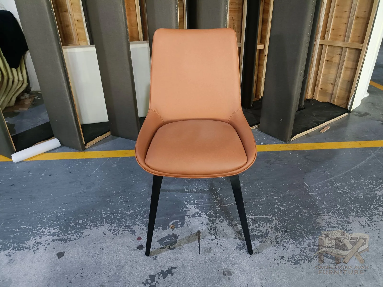 A tan padded shell seat stands on four slim dark legs.